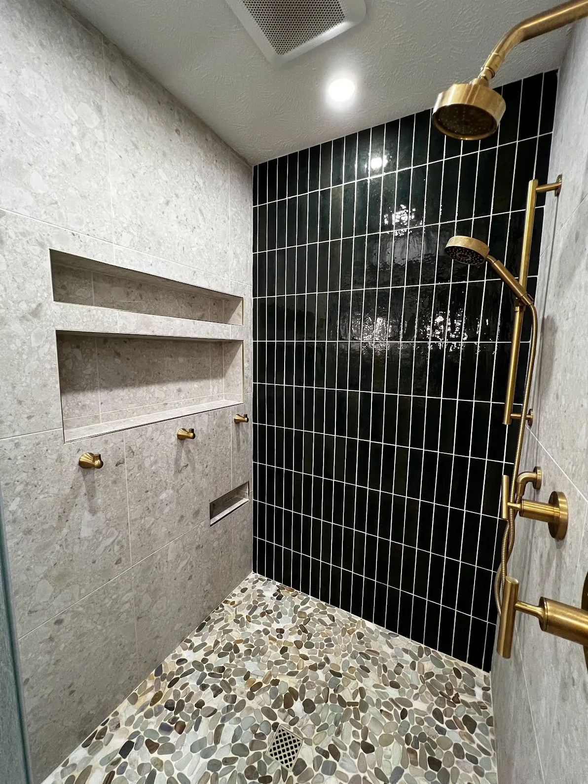 Walk-in shower with black tile, gold fixtures, and pebble floor