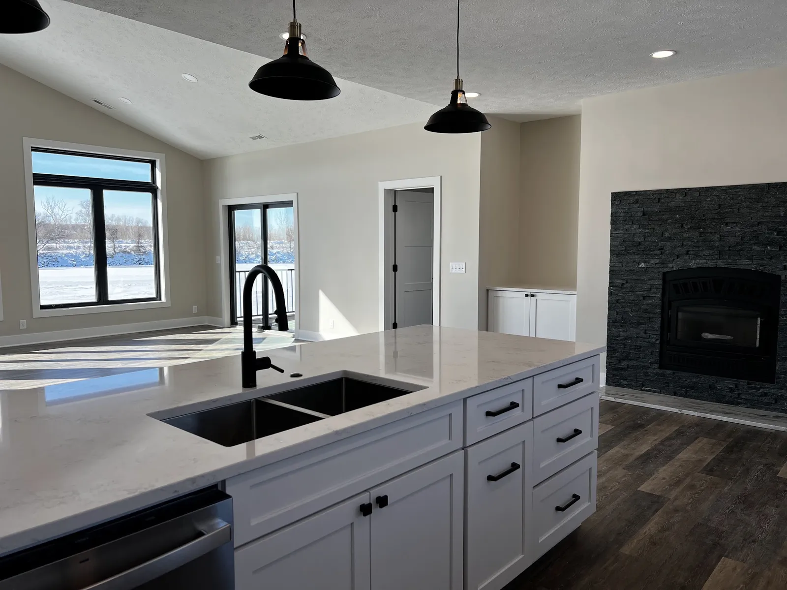 White kitchen remodel with quartz island, black pendants, and stone fireplace