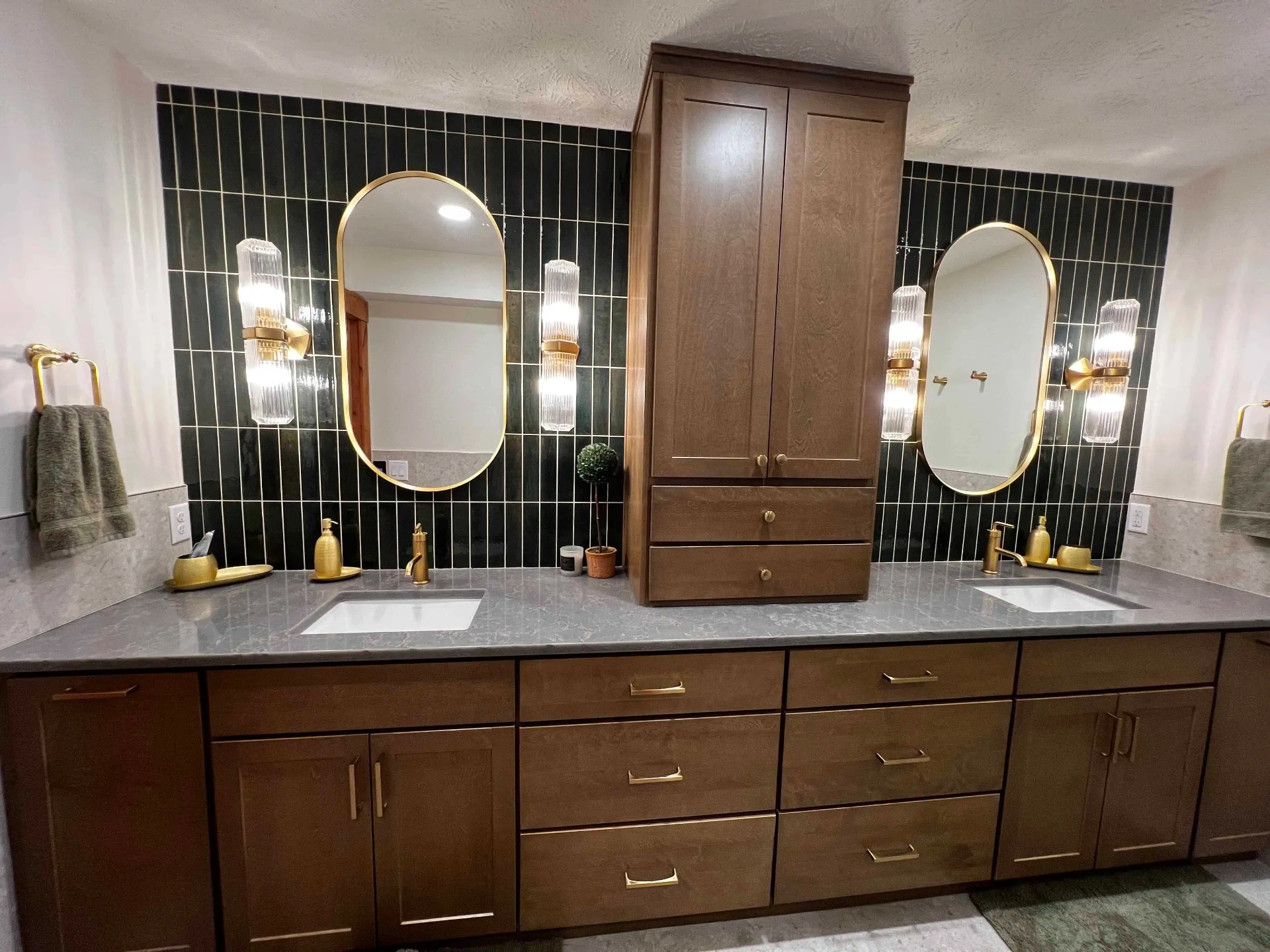Double vanity bathroom remodel with dark green tile, gold fixtures, and oval mirrors